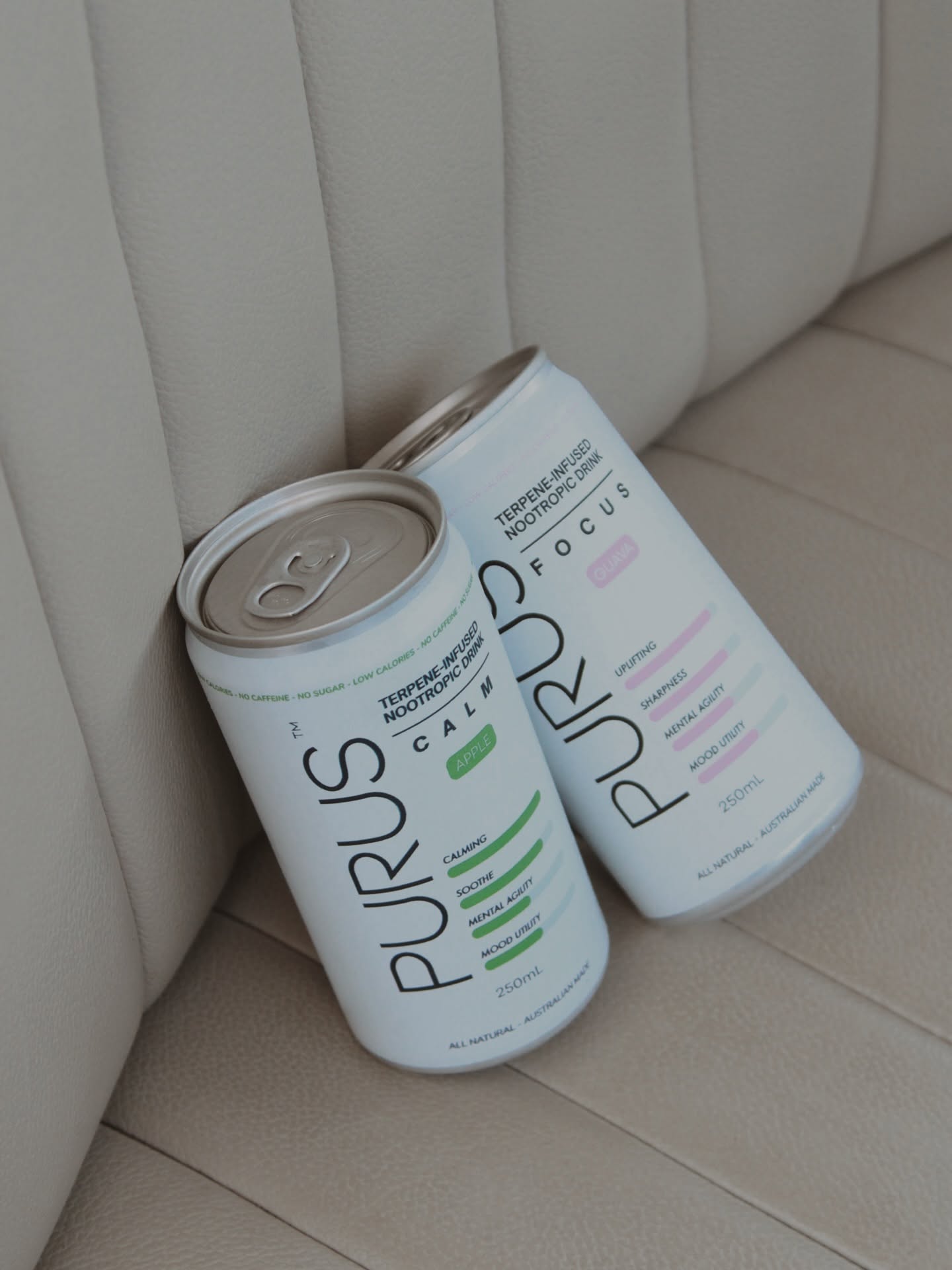 Two white cans of cold drink resting against a cream seat