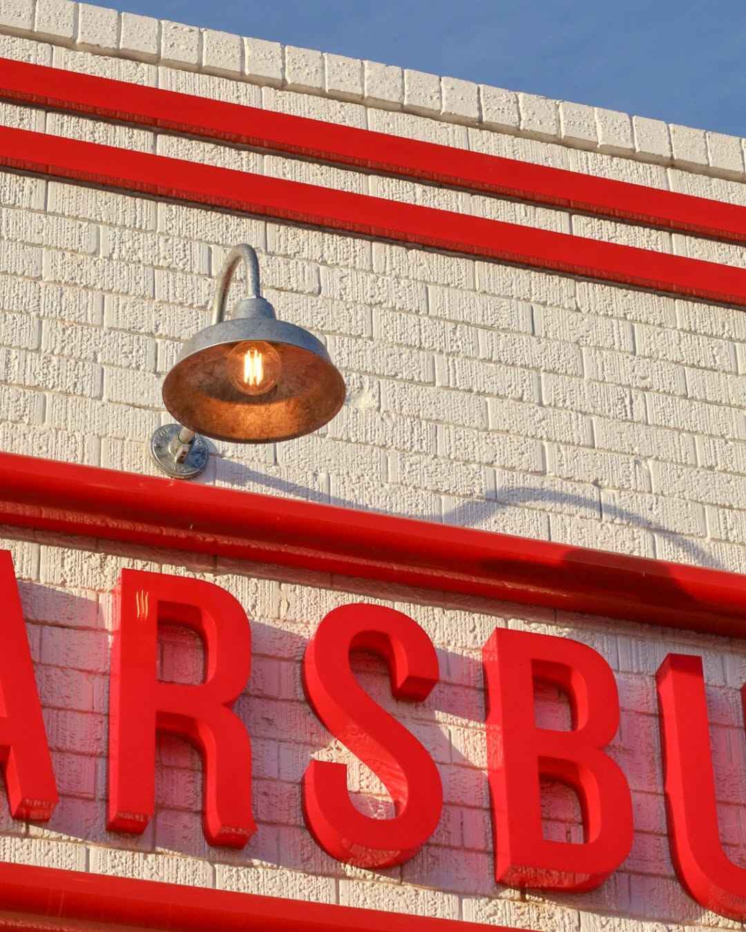 White painted brick wall with red trim and a galvanised gooseneck lamp glowing warmly at the Liberty Mullumbimby station