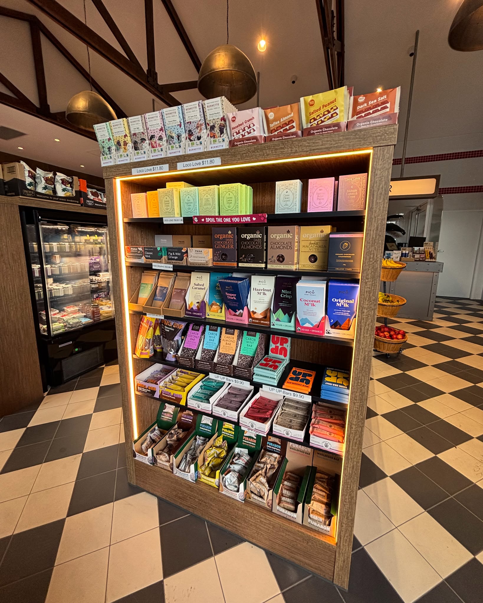 Warmly lit wooden shelf stocked with packaged snack bars and chocolate inside the Liberty Mullumbimby store